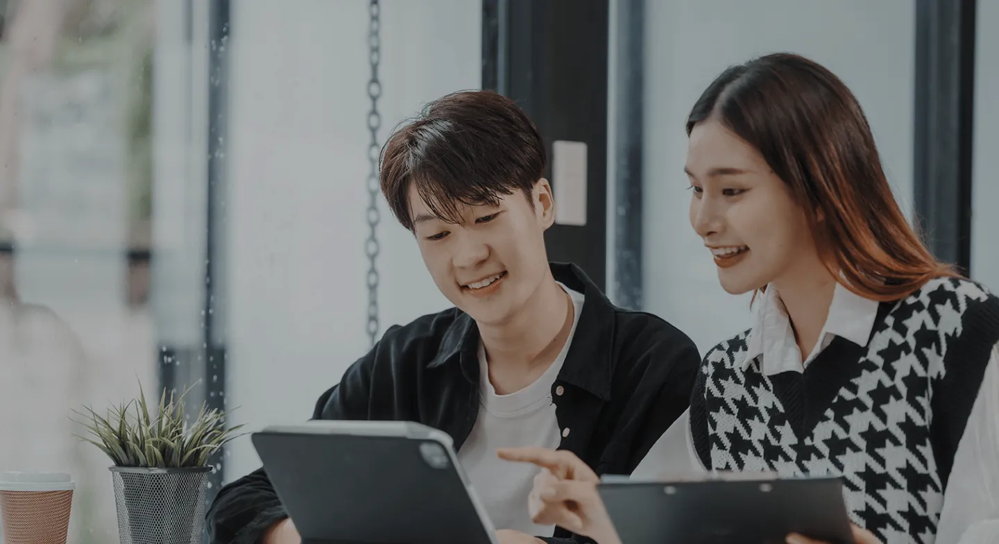 젊은 남녀가 태블릿을 보며 무언가를 손가락으로 가리키고 있는 사무실 안의 장면입니다.